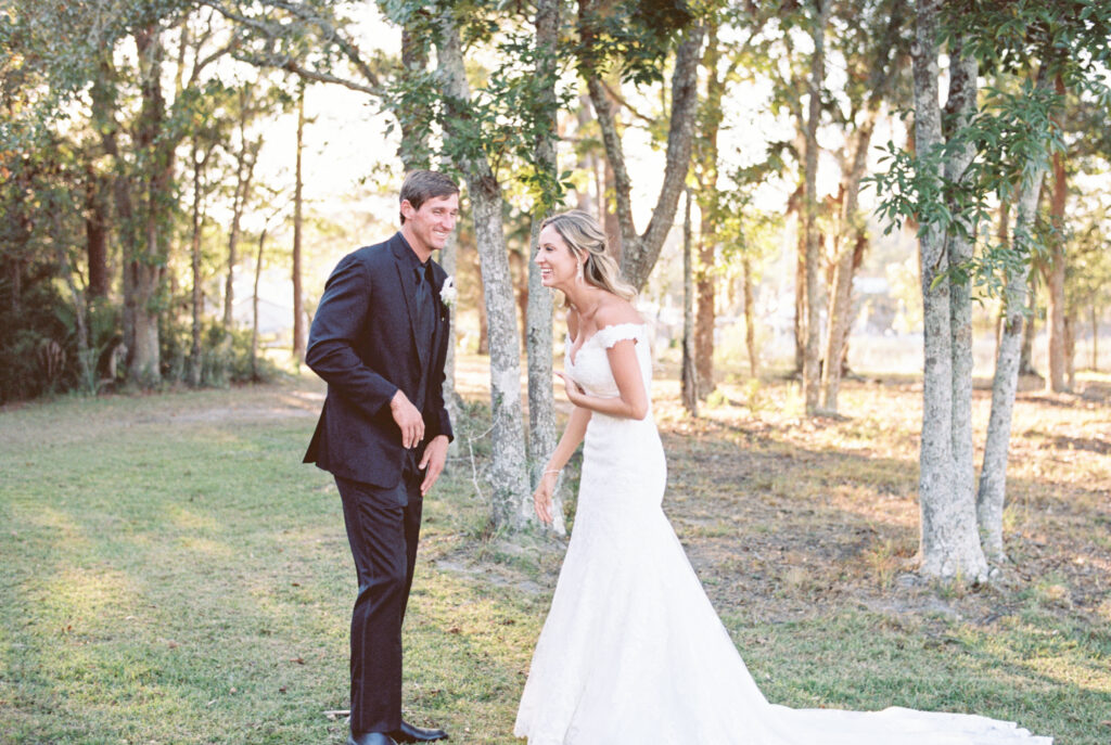 Bride and groom laughing at each other during their micro wedding in Charleston SC. Bride wearing an off the shoulder white dress and groom in all black tux