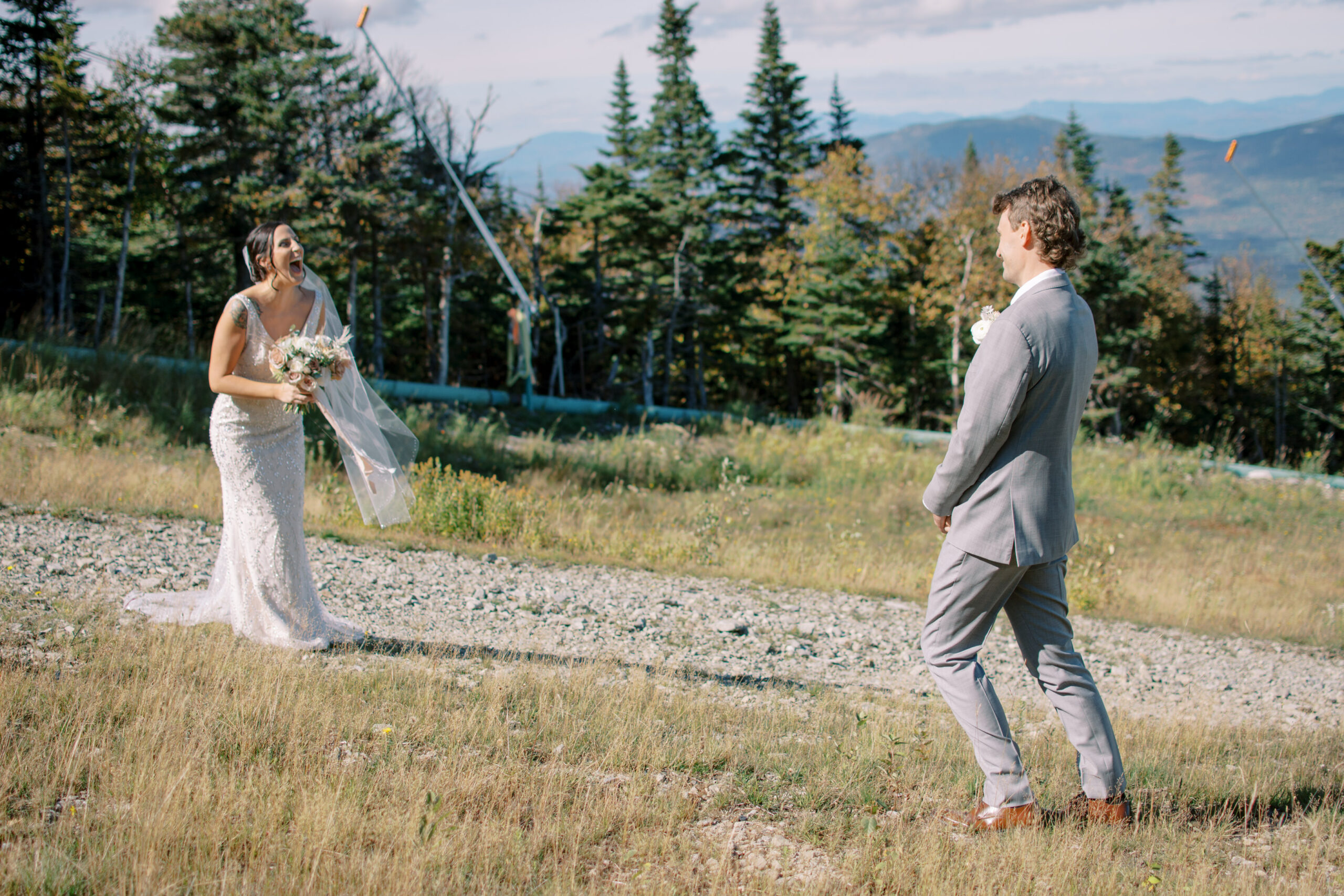 Bride and groom on a mountain top at a ski resort laughing at each other during their first look