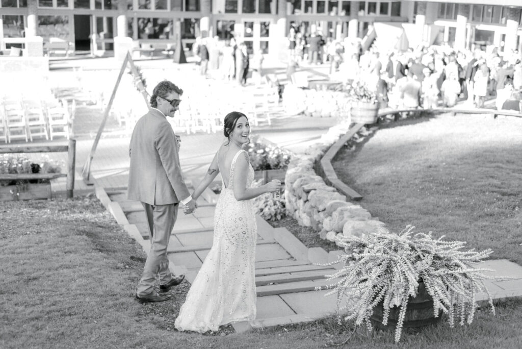 Black and white portrait of bride and groom holding hands and walking down a stone path at Sugarloaf USA