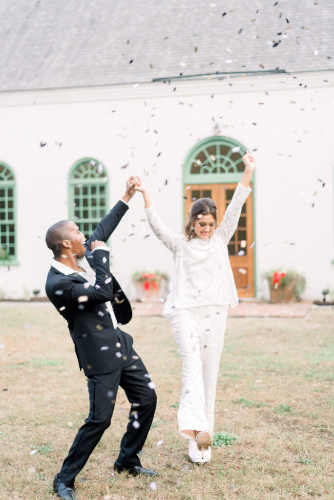 Bride and groom celebrating under confetti bride wearing a lace pantsuit