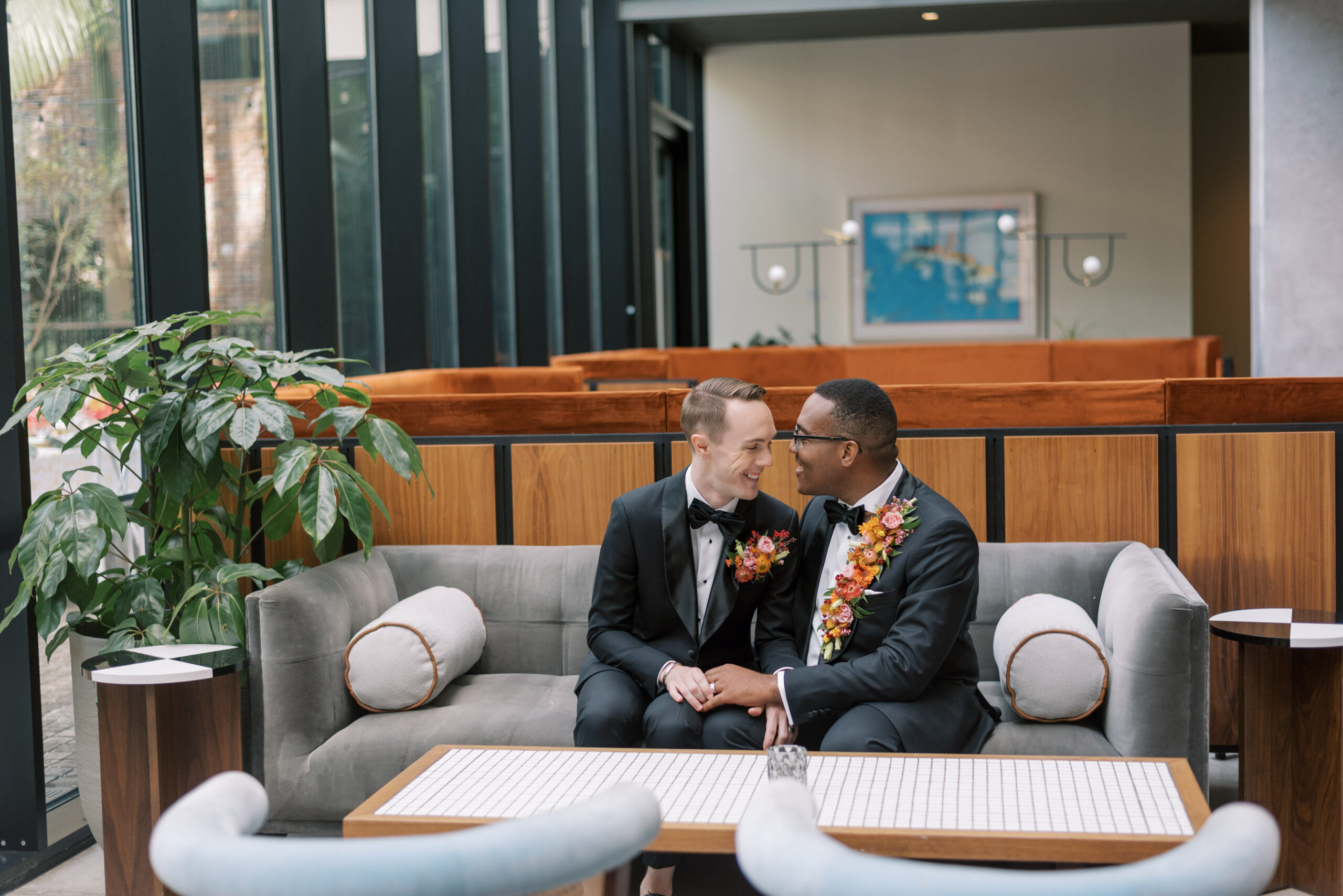 two men sit side by side sharing a quiet moment on their wedding day dressed in black tuxes from Indochino at Hotel Haya in Tampa Florida