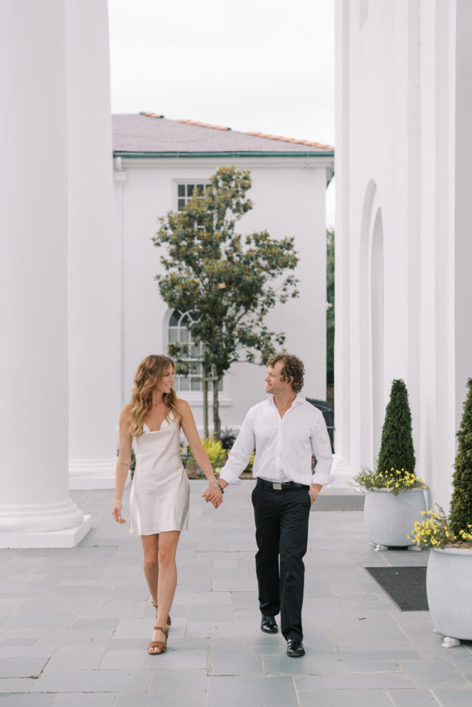 Engaged couple hold hands and smile at each other walking towards the camera