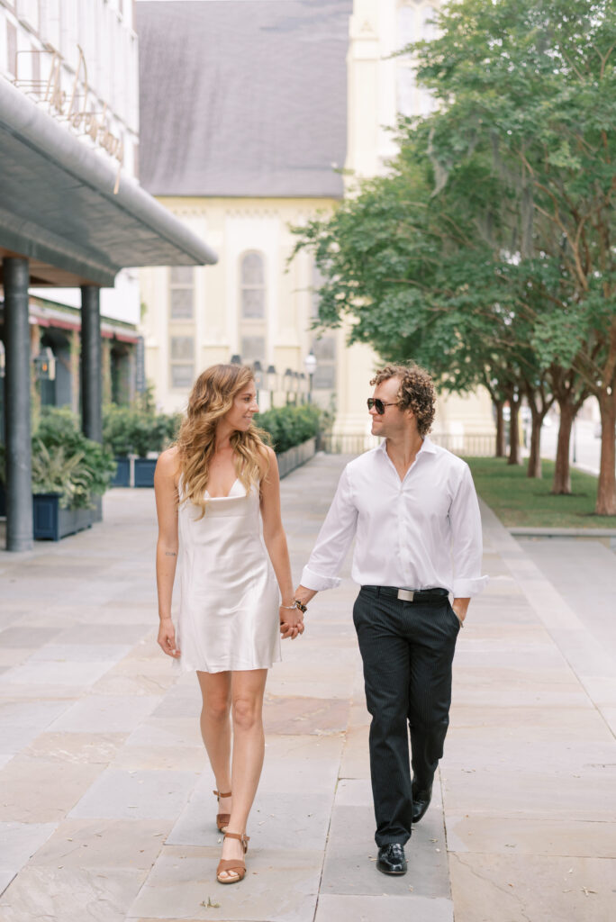 engaged couple hold hands and walk down the sidewalk in front of The Dewberry