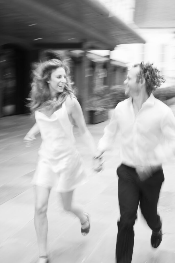 black and white motion blur image of an engaged couple holding hands and running together