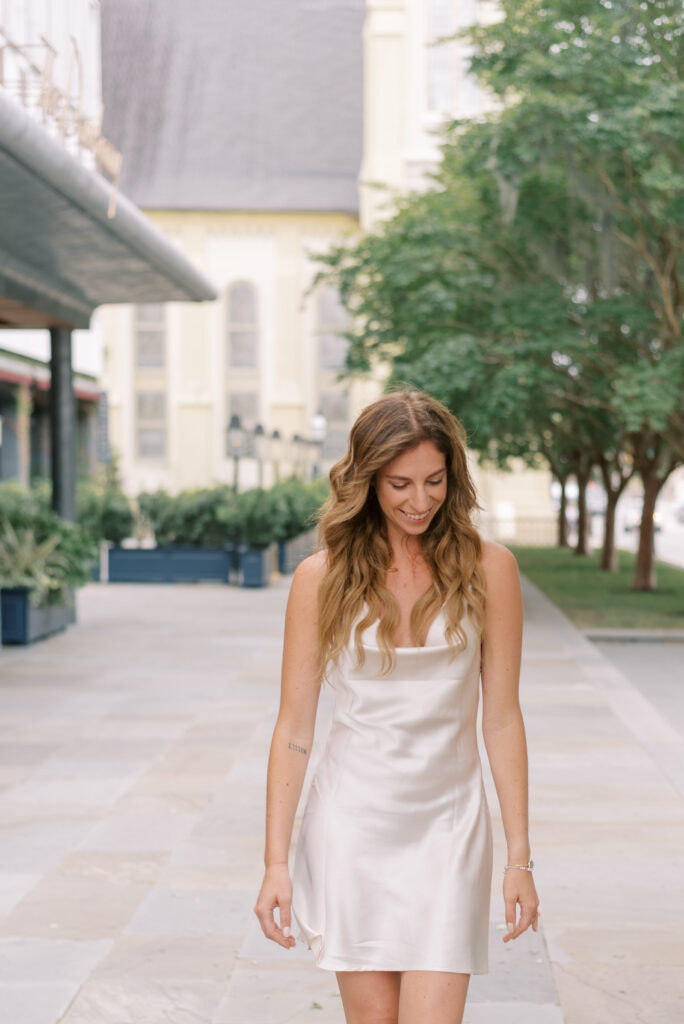 woman smiles at the ground in a white slip dress