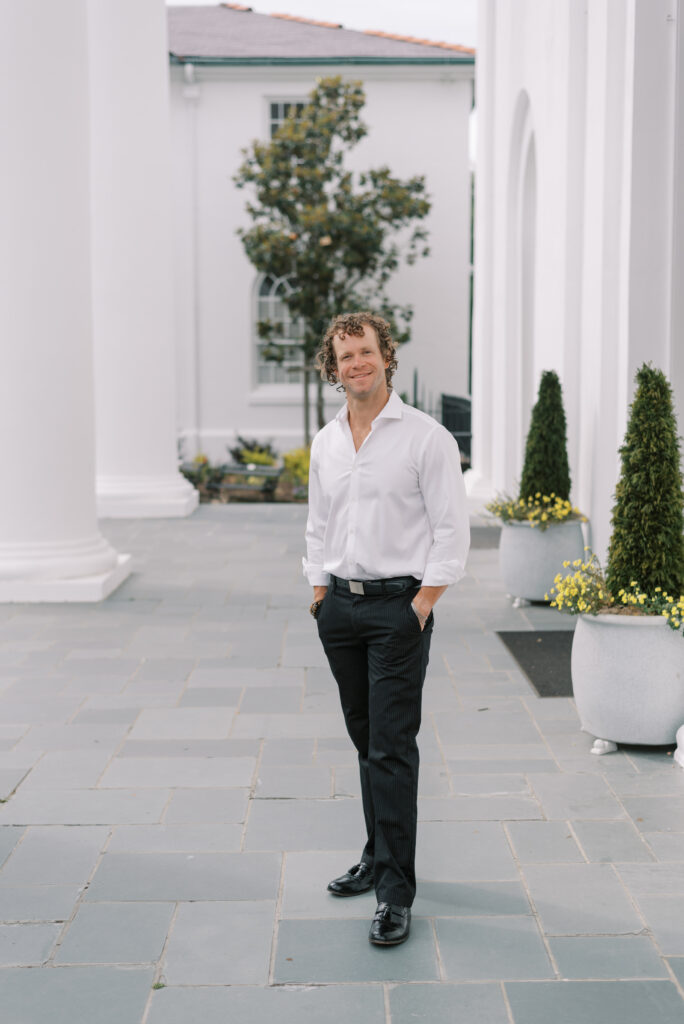 man in white shirt and black slacks smiling on a church porch in Charleston