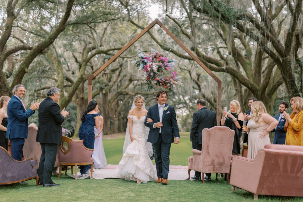 Married couple walk arm and arm away from their wedding ceremony at the avenue of oaks