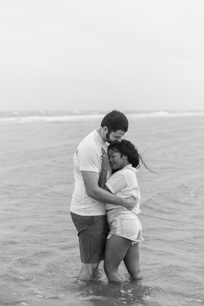 couple hugging while they stand knee deep in the ocean captured in black and white