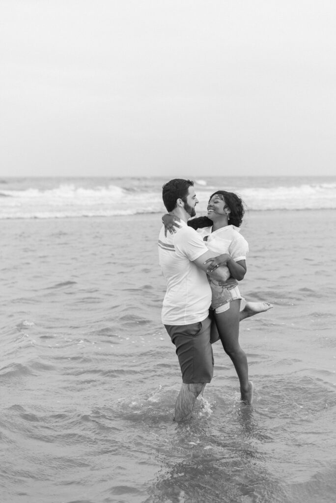 man spinning his fiance around while in the water captured in black and white