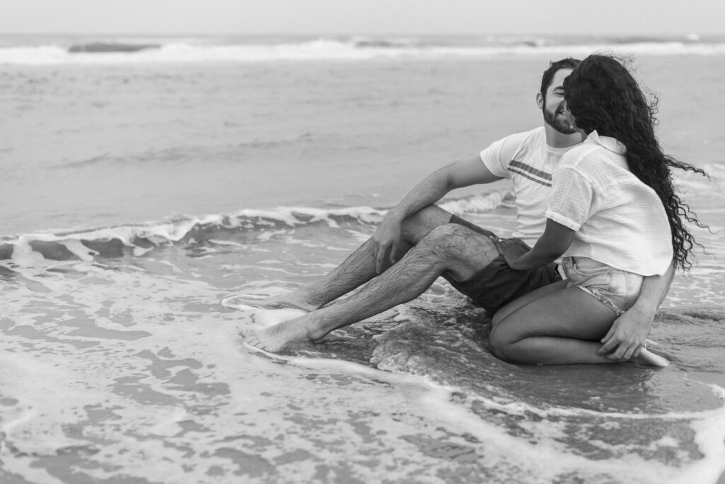 couple sitting in the water while smiling together captured in black and white