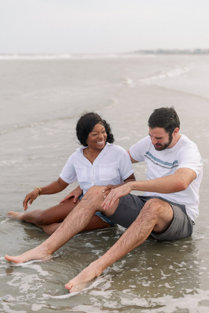 Couple splashing water on each other sitting in the waves