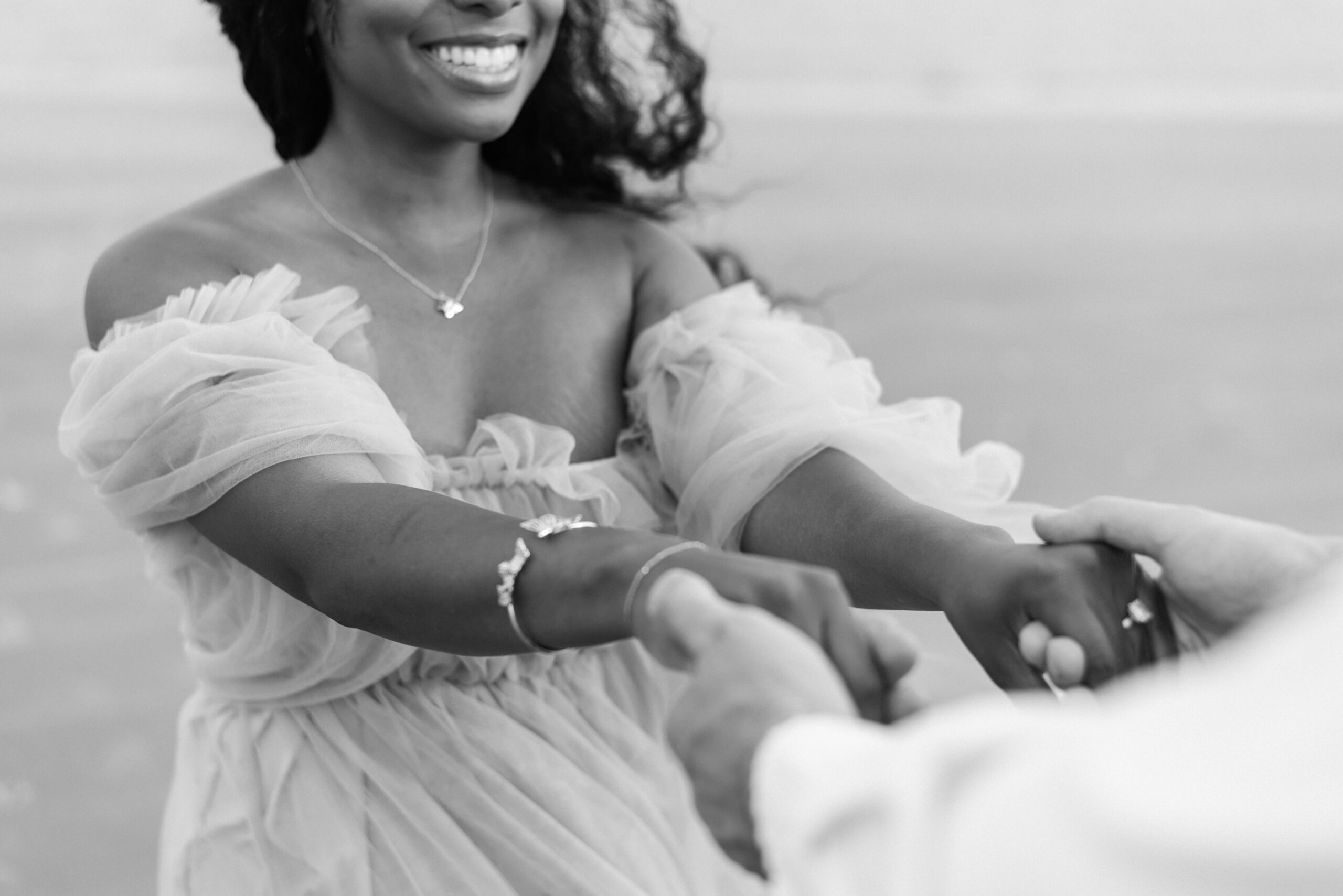 Black and white image of an engaged couple holding hands and spinning on the beach