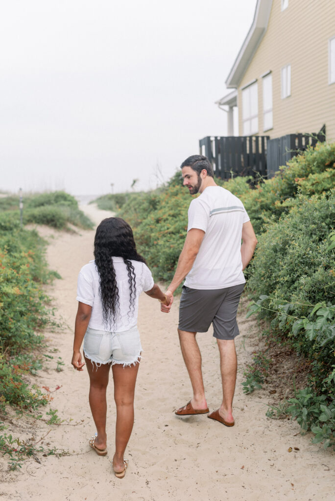 An enchanting moment captured on camera as an engaged couple strolls hand in hand down a sandy path, their destination set on the majestic ocean at Isle of Palms Beach. With each step, love and anticipation fill the air, creating a timeless scene of romance and connection. The sandy path invites them to embark on a journey together, guided by their shared dreams and the allure of the vast ocean ahead. This captivating photograph depicts the joy and unity of the couple's bond as they traverse the path of love towards a future filled with endless possibilities.