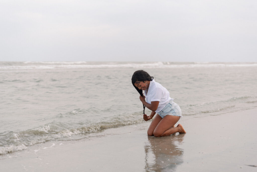 Woman kneeling in the sand at Isle of Palms beach getting her hair wet in the ocean