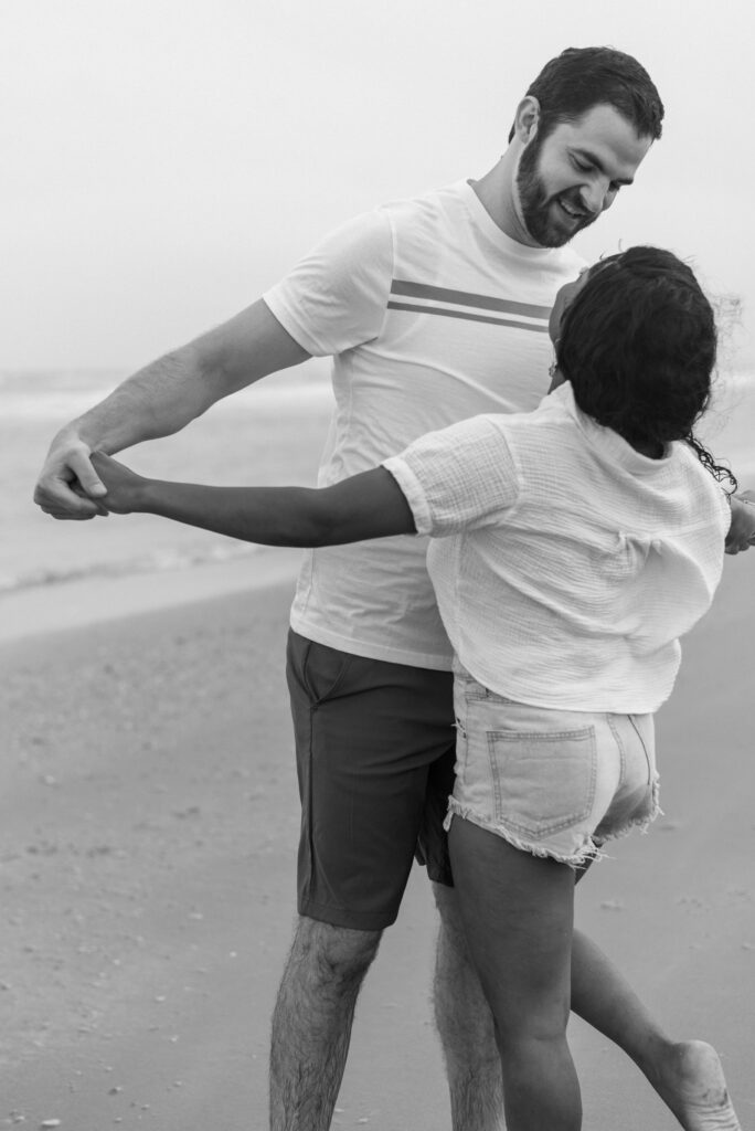 engaged couple playing together on the beach holding hands captured in black and white