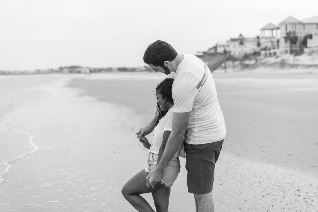 Black and white image of an engaged couple laughing and leaning against each other 