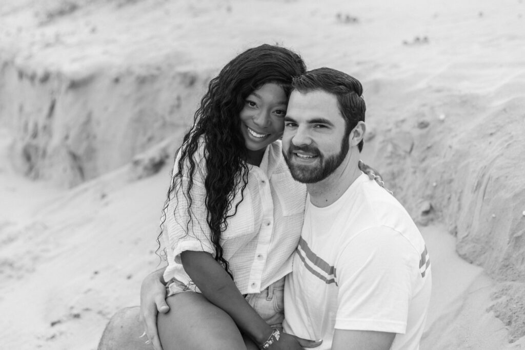 black and white portrait of an engaged couple sitting in the sand