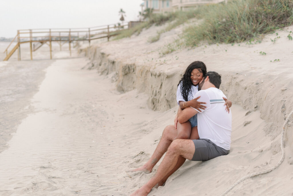 couple sitting in the sand, she is sitting on his lap and they're snuggling together