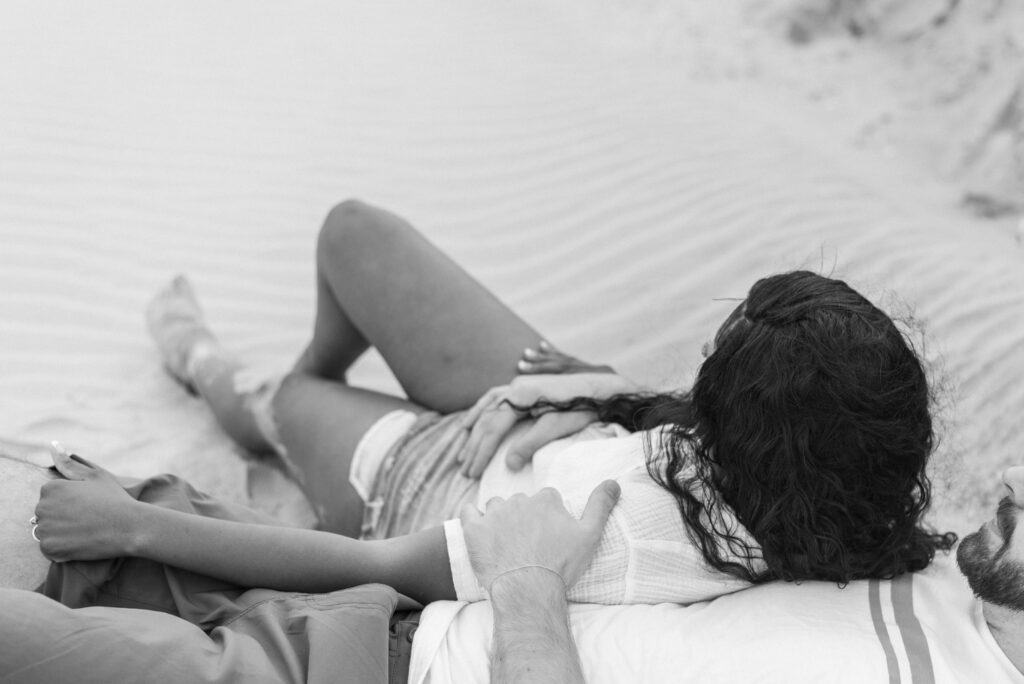 black and white image of a couple lounging together in the sand 