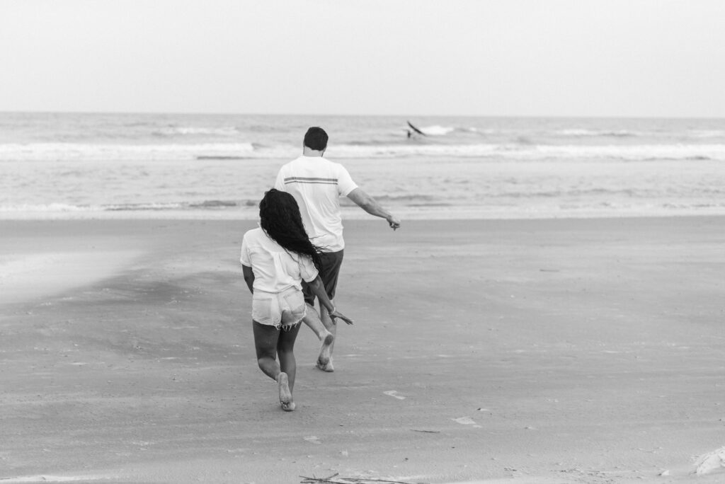 couple running on the beach towards the water captured in black and white