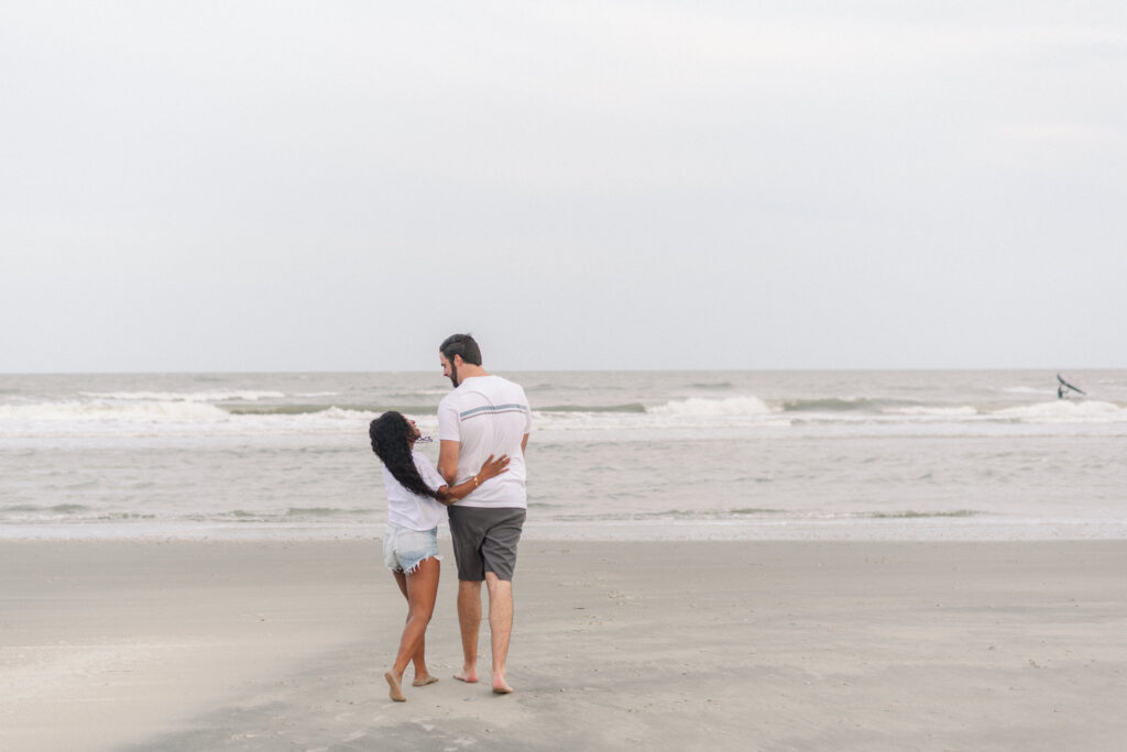 couple walking on the beach smiling at each other walking towards the water