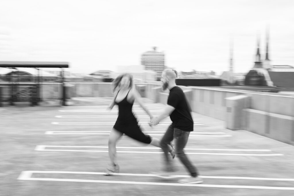 black and white motion blur image of a man and woman holding hands and running on top of a parking garage