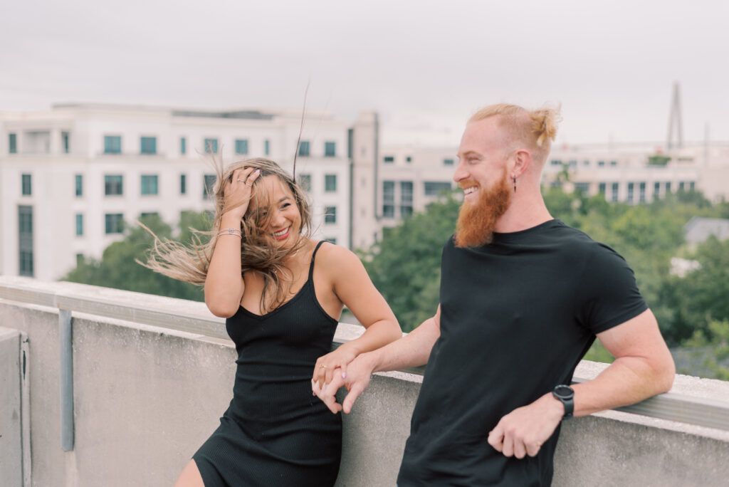 couple laughing at each other while the woman fixes her hair on a parking garage