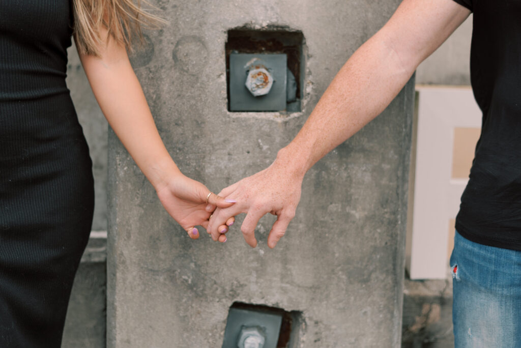 close up of a couple holding hands in front of a concrete wall