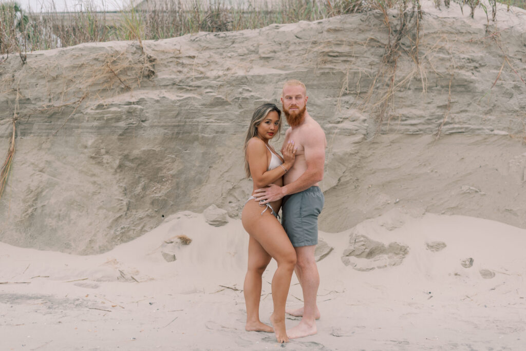 couple in swimwear stand together in front of a sand wall at isle of palms beach