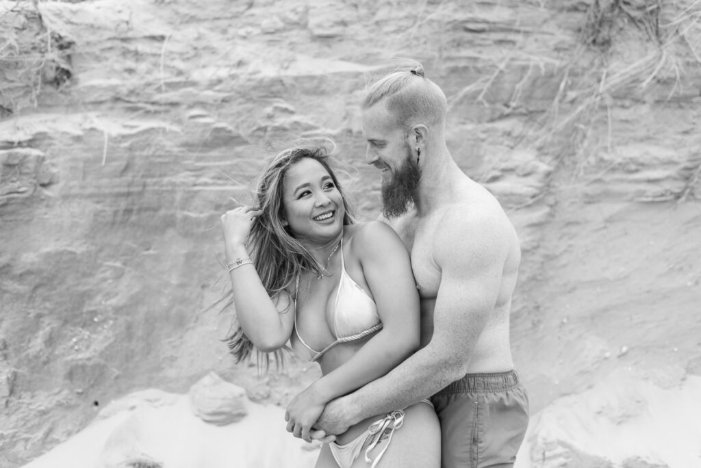 black and white portrait of a couple in swimwear smiling at each other in front of a sand wall