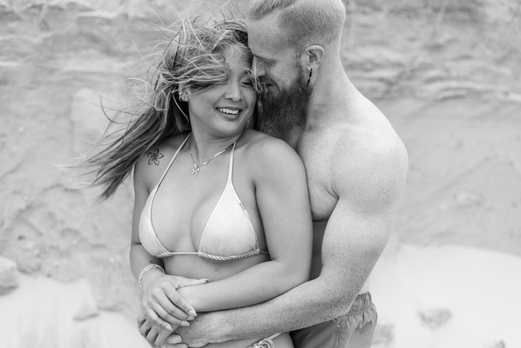 black and white portrait of a couple hugging while the wind blows her hair around