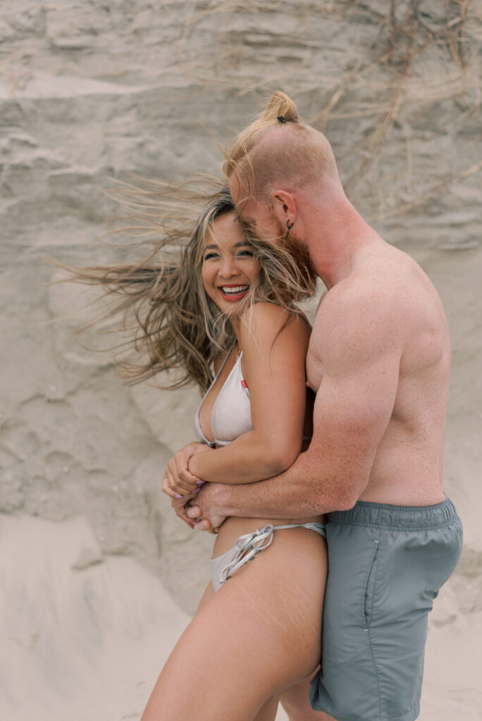 couple embracing and laughing at each other in front of a sand wall on isle of palms 