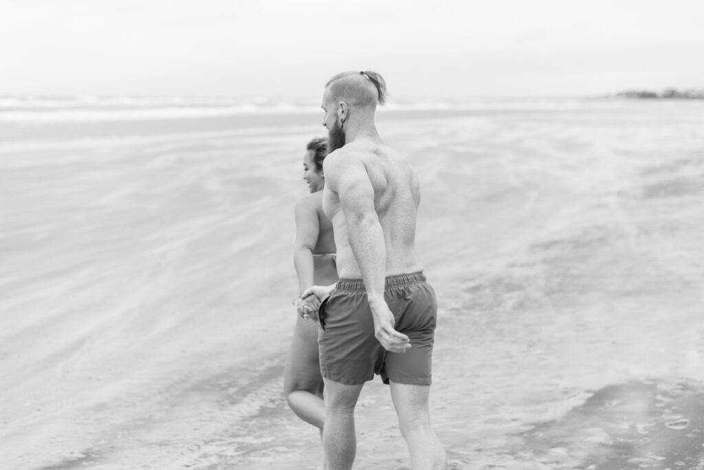 couple running across a windy beach while sand blows