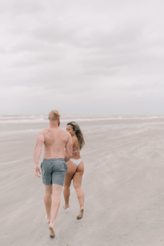 couple running across a windy beach while sand blows