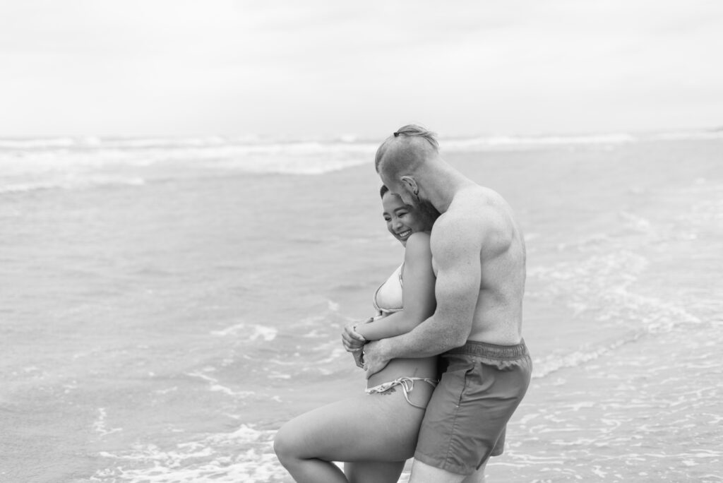 woman leans back into her boyfriend and laughs as they stand in the ocean