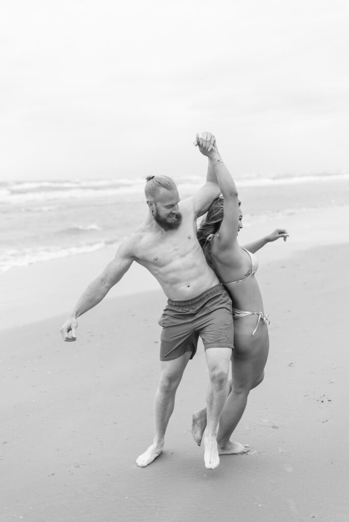 couple bumping hips and laughing while they walk down the beach