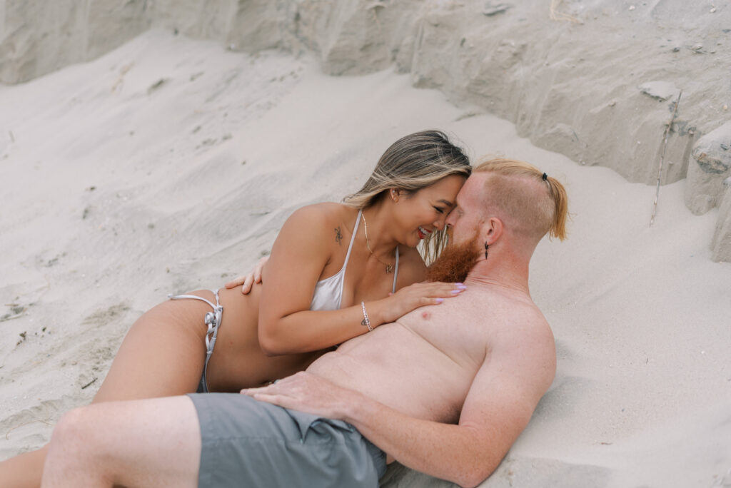 couple laying in the sand together and pressing their foreheads together