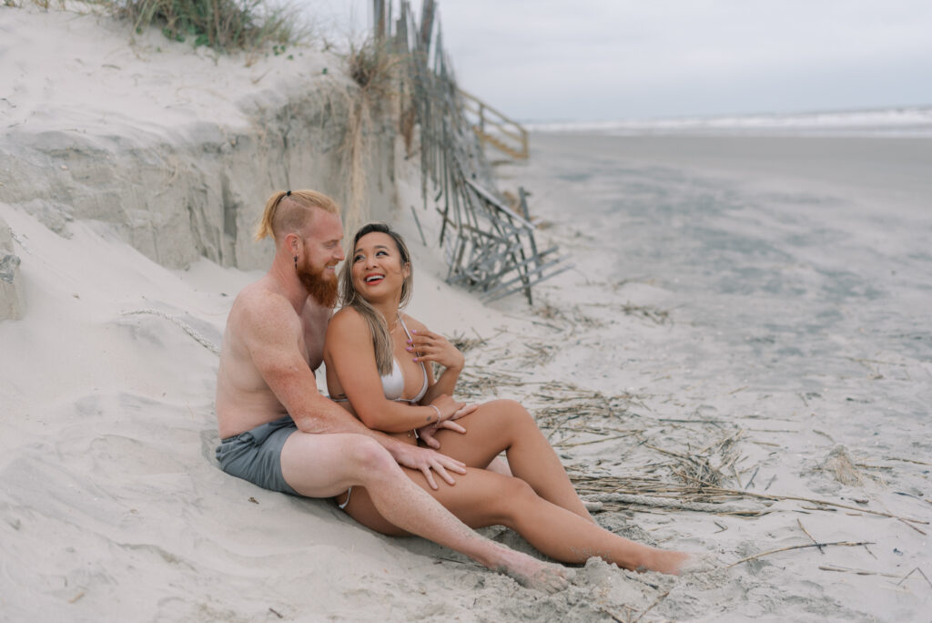 couple sitting together in the sand in front of a collapsed sand fence