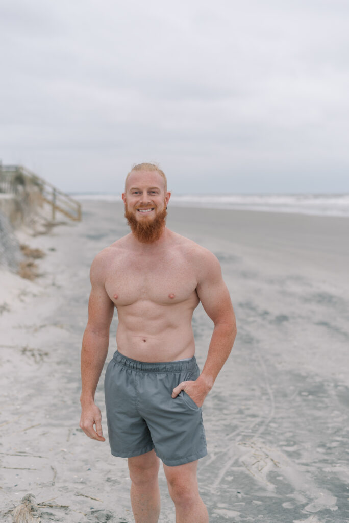 portrait of a man smiling at the camera with a red beard and gray swim shorts