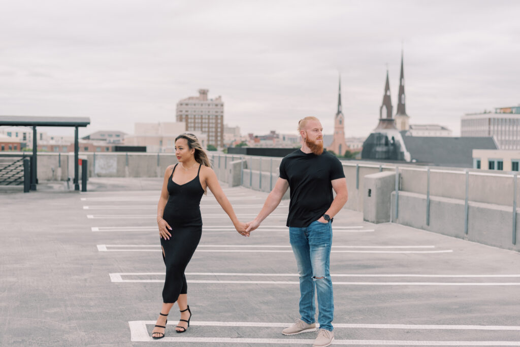 man and woman holding hands looking away from each other on top of a parking garage in Charleston