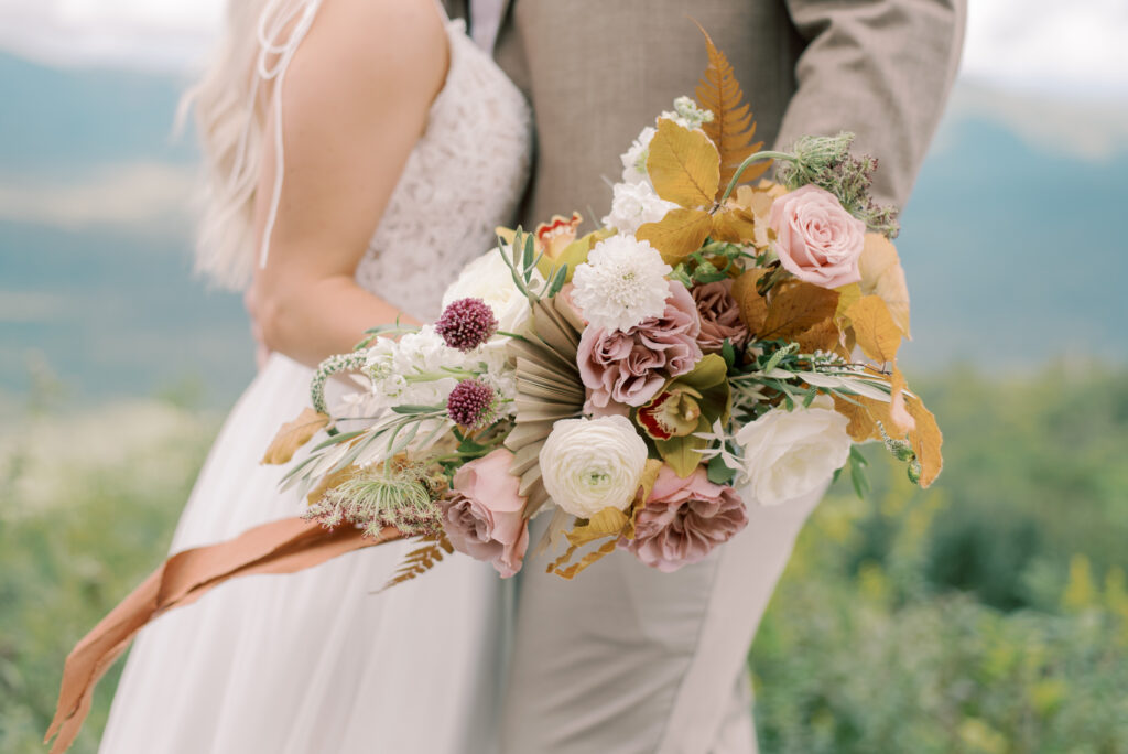 Eloping couple standing together holding an autumn wedding bouquet with roses and dried flowers