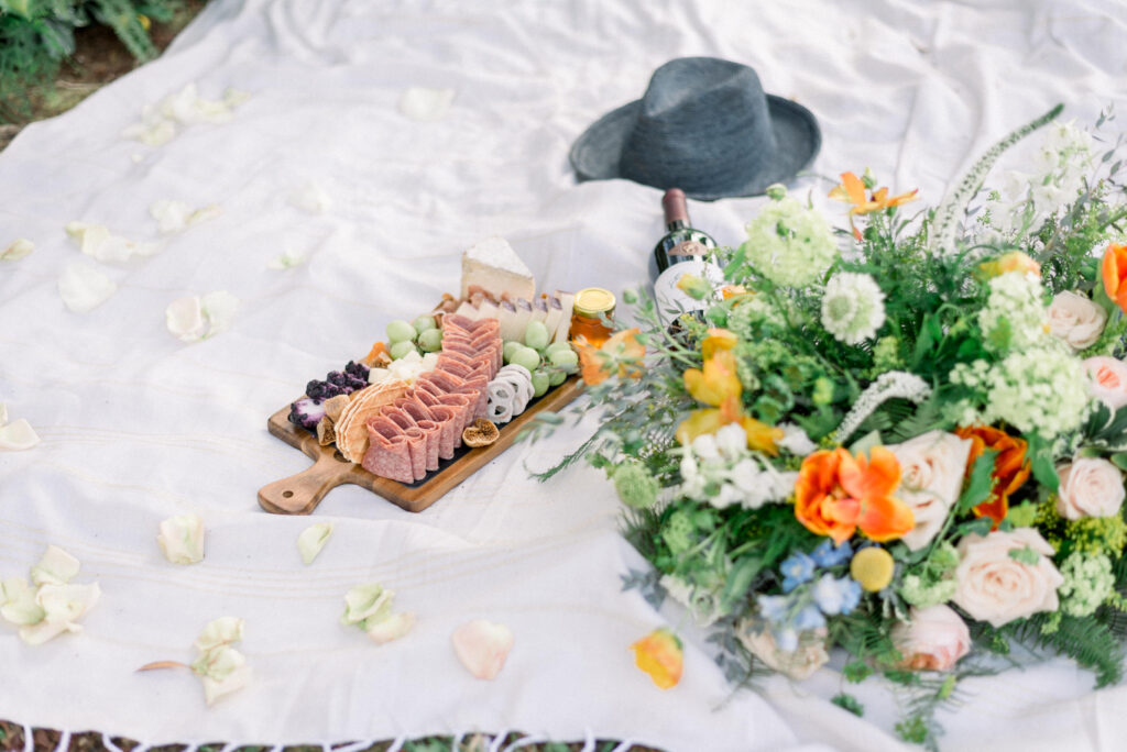 charcuterie board on a blanket with summery flowers an the grooms hat at an intimate wedding