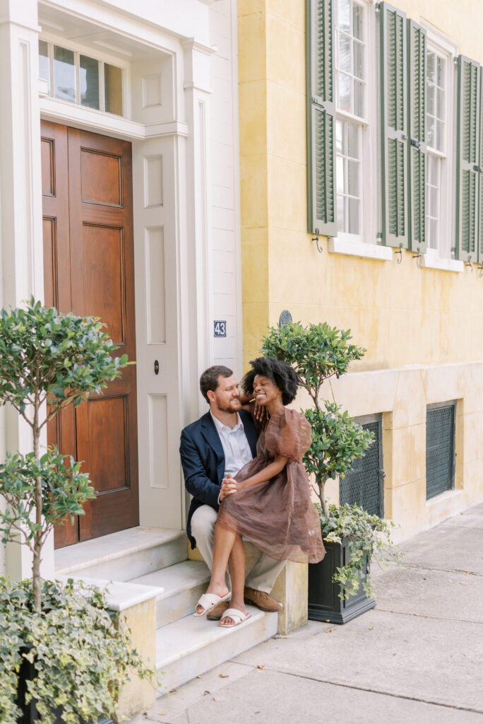 woman sits on her boyfriend's lap during engagement photos