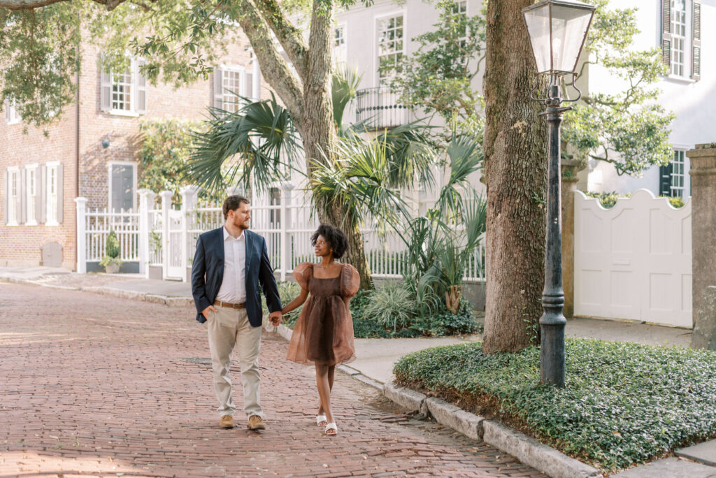 Couple holding hands walk down a brick road in historic Charleston