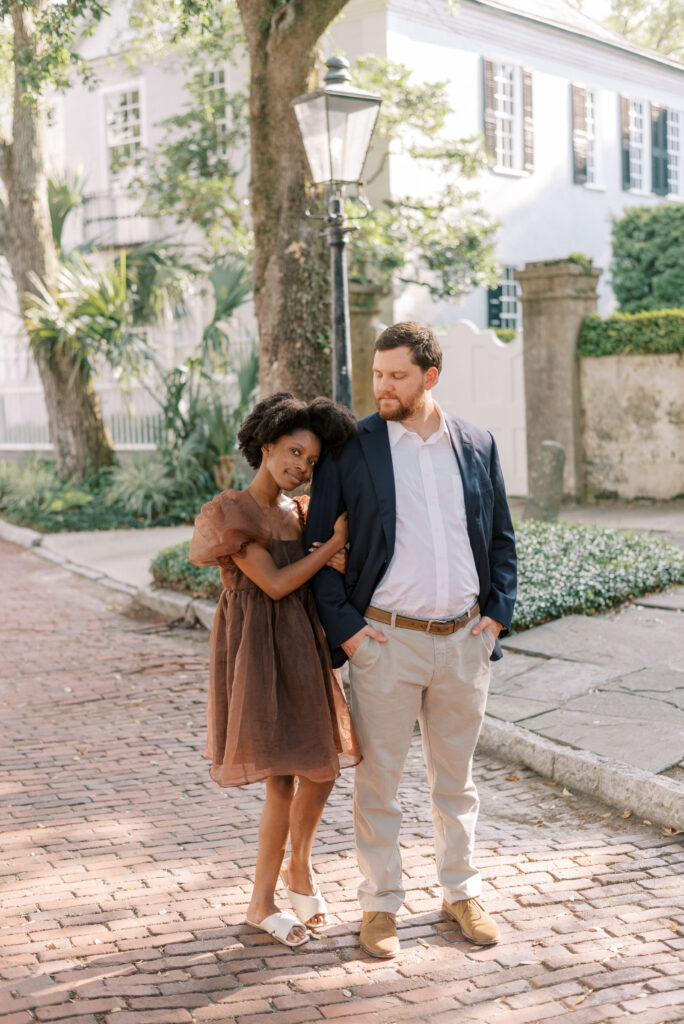 Woman lays her head on her fiancé's shoulder while they stand on a brick road