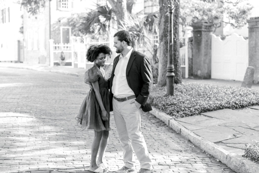 Black and white portrait of a couple smiling together on a brick street in Charleston