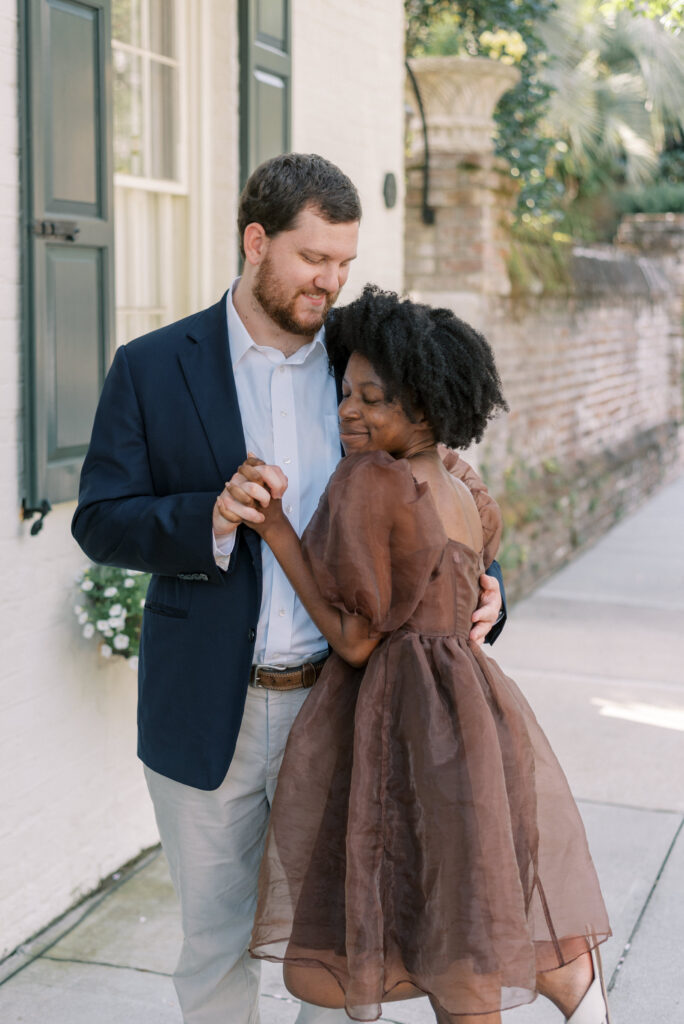 Man in a navy suit jacket and woman in a brown tulle dress hug