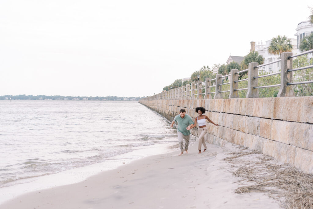 couple holds hands and runs on the beach in downtown Charleston