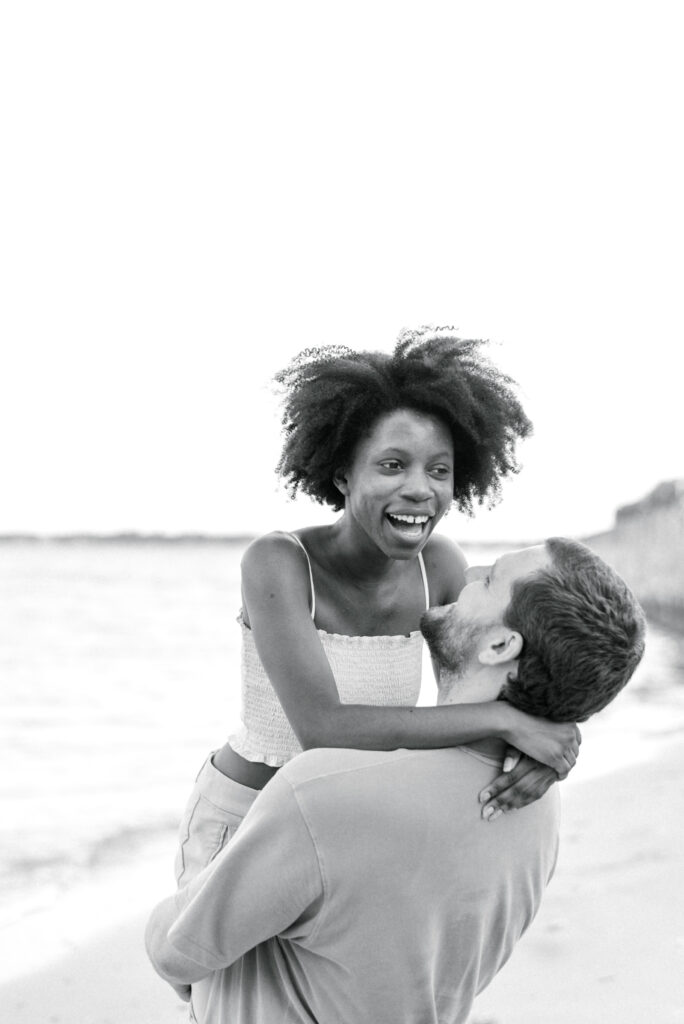 woman laughs while her boyfriend spins her on the beach in Charleston