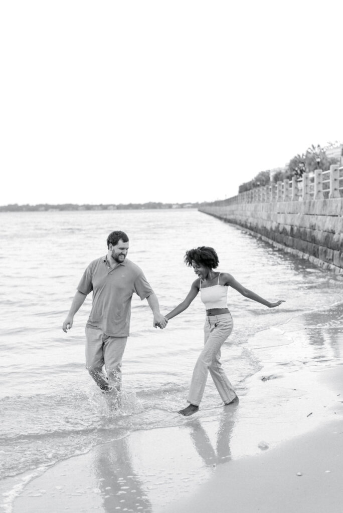 couple hold hands and walk through the water kicking it at each other 